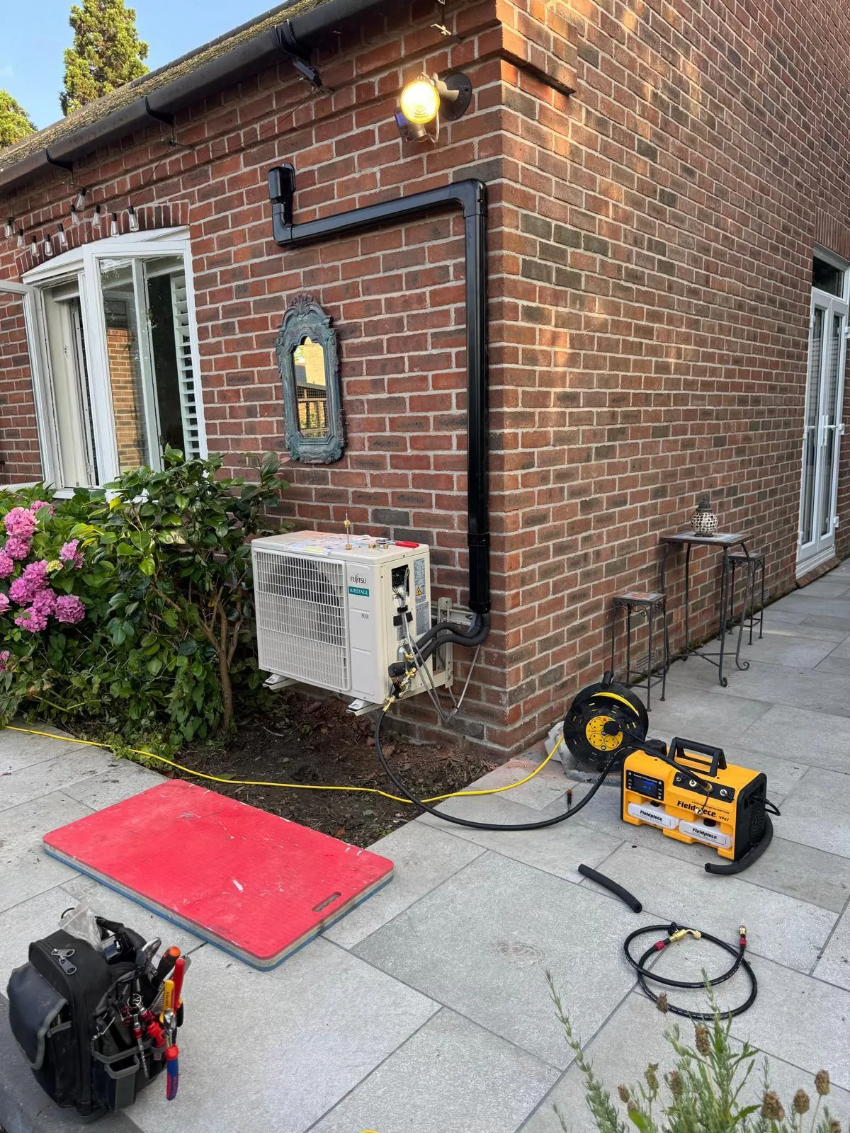 Fujitsu air-conditioning outdoor unit mounted on a brick wall with black trunking, on test with Fieldpiece gauges